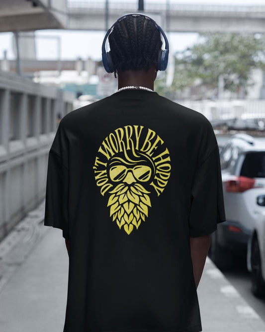 Person wearing a black t-shirt with yellow graphic and text, walking outdoors.